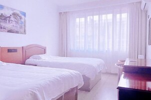 A hotel room with two beds, a painting on the wall, a window with curtains, and a desk with a chair.