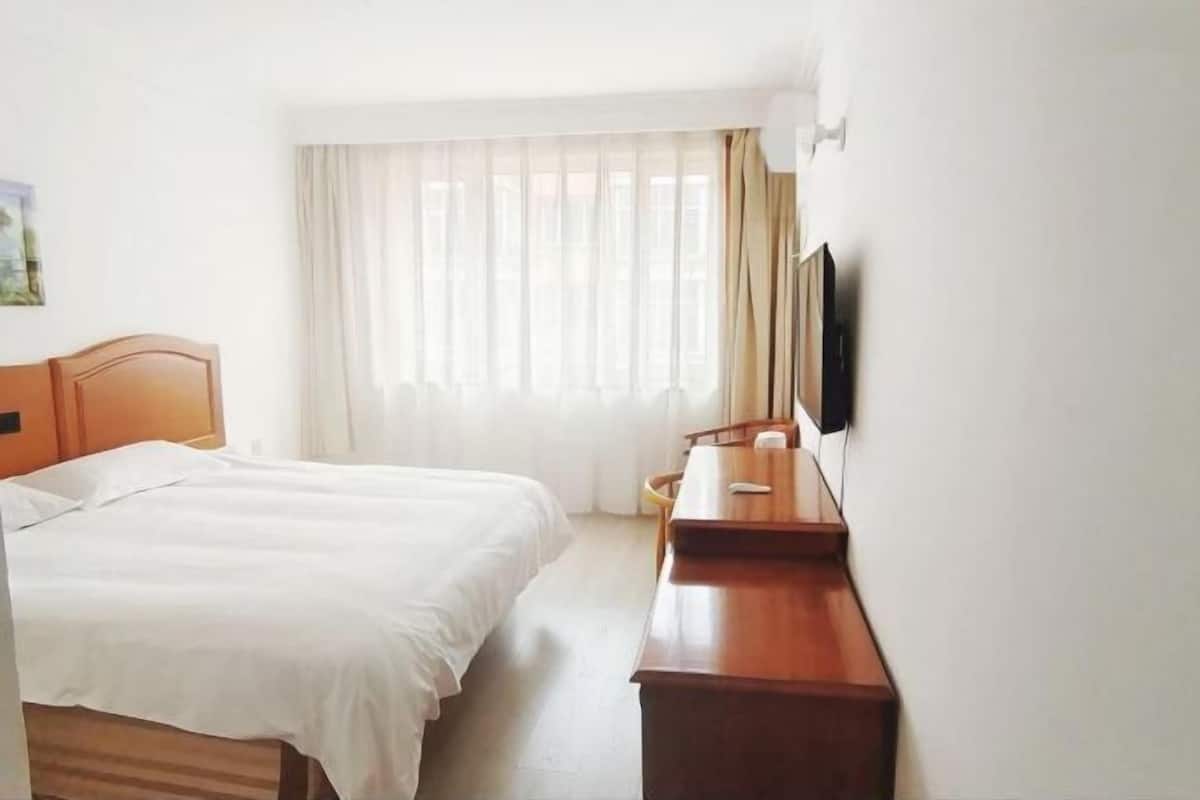 A hotel room with a bed, a desk, and a TV mounted on the wall.