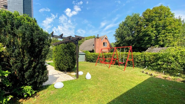 A well-maintained garden with a swing set, a pathway, and a brick house in the background. - Heavenly vacation home near the sea (Bruinisse)