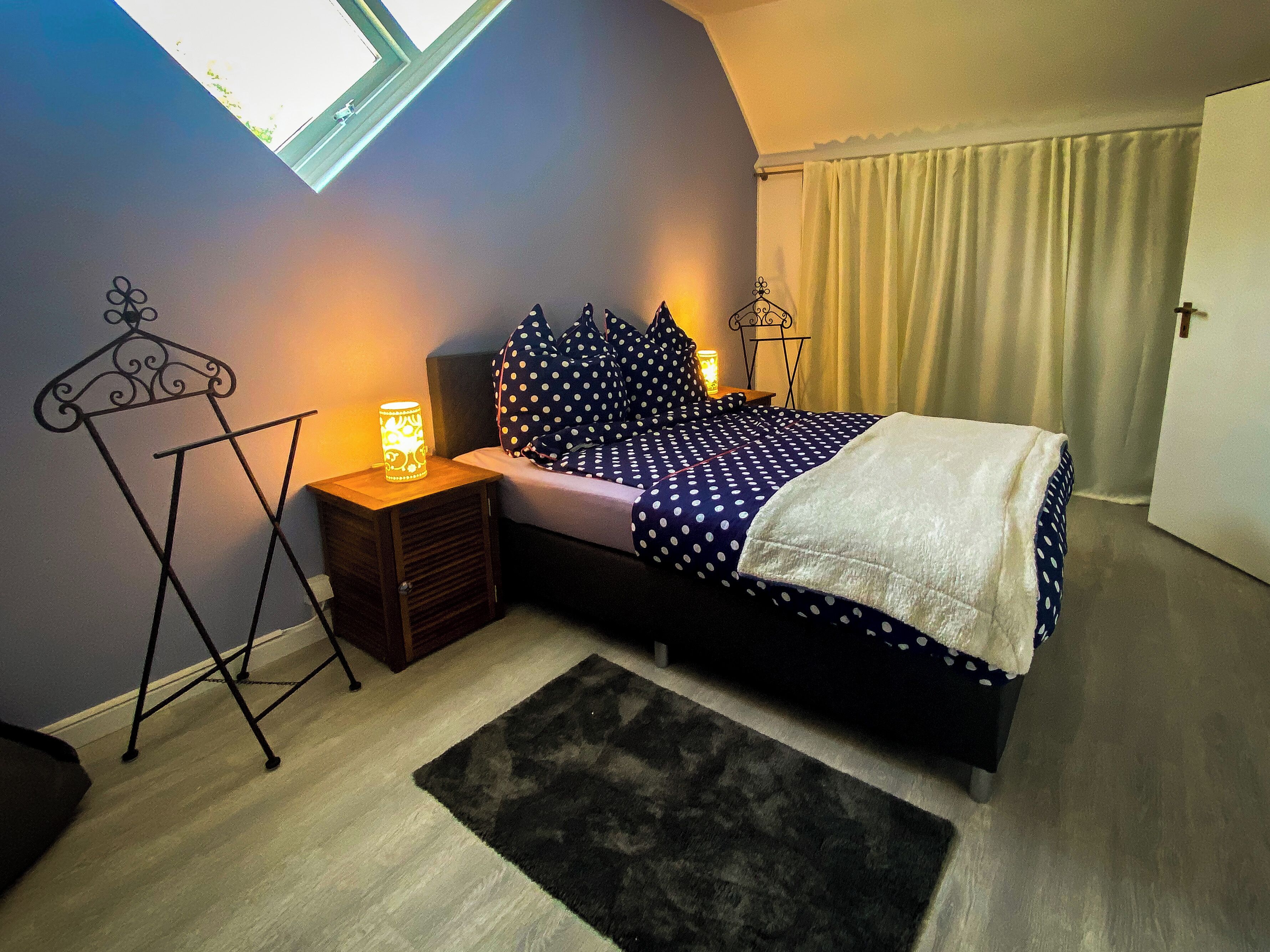 A bedroom with a bed, a nightstand, a lamp, a window, and a door.