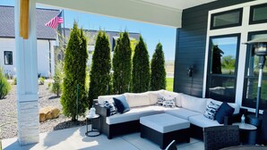 An outdoor patio with a sectional sofa, a round table, and tall conifer trees.