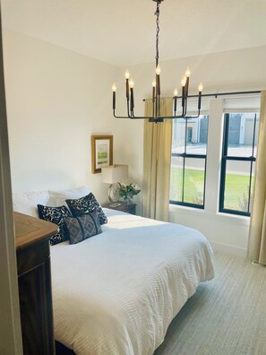 A bedroom with a large bed, a chandelier, a bedside table with a lamp, a framed picture, and a window with a view of the outside. - New Luxury Escape, Mountain Views, Pool & River Access!  (Star)