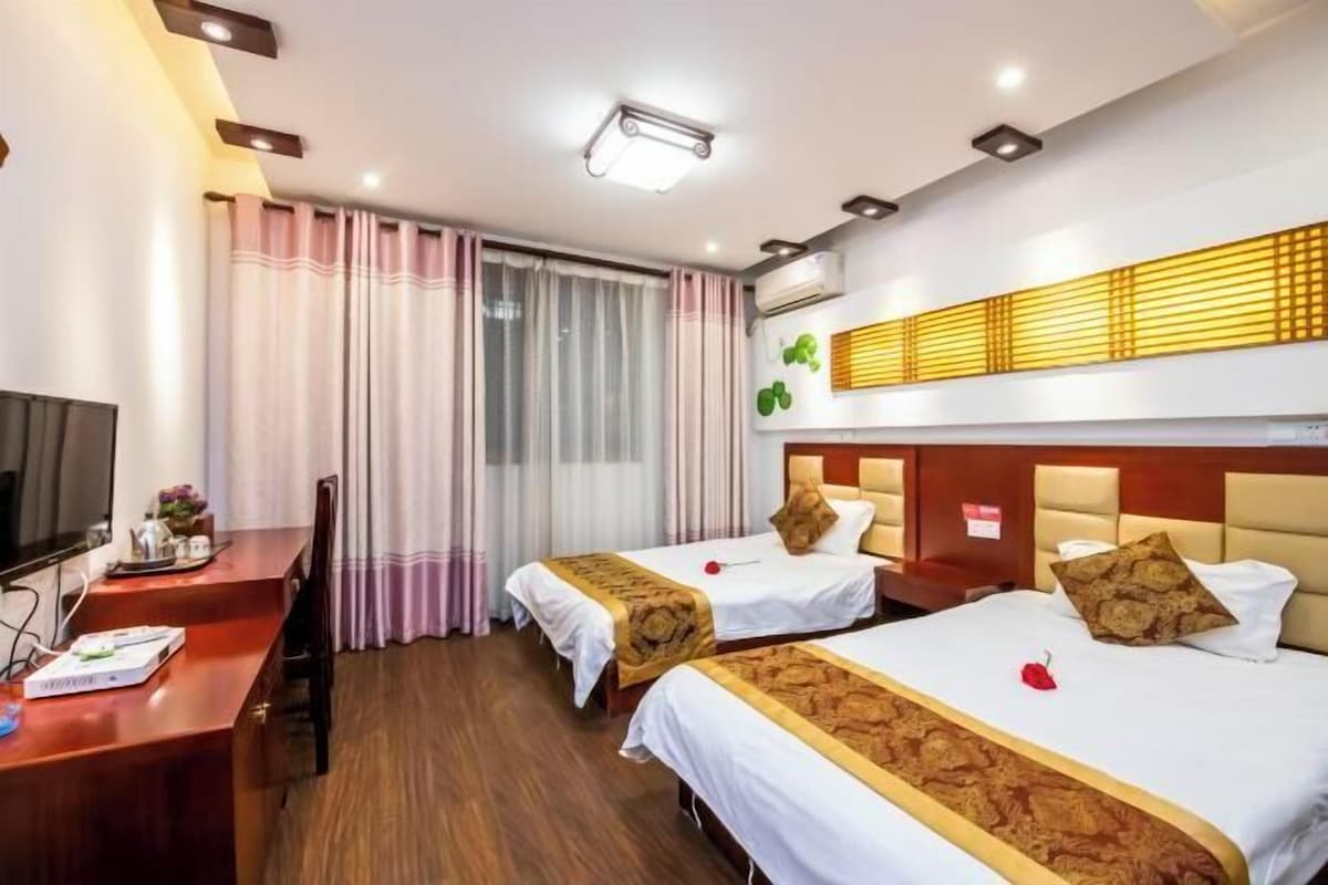 A hotel room with two beds, a desk, a TV, and a window with curtains.