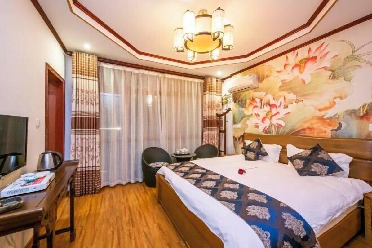 A hotel room with a large bed, a desk with a chair, a small table, and a painting on the wall.