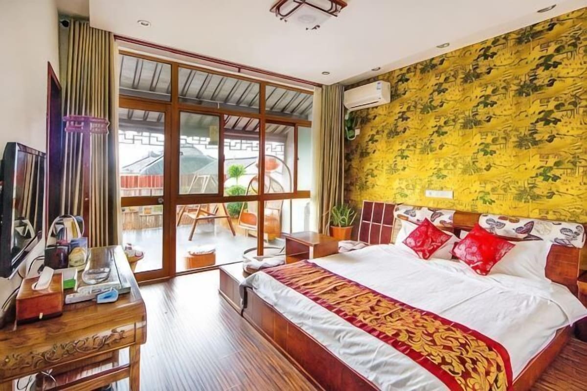 A hotel room with a large bed, a television, a desk, and a sliding glass door to the outside.