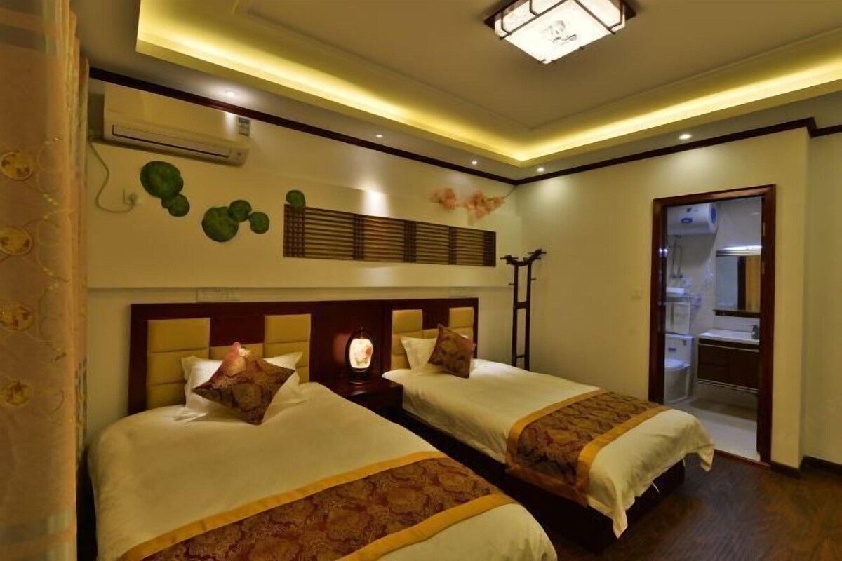 A hotel room with two beds, a ceiling light, an air conditioning unit, and a bathroom visible through an open door.