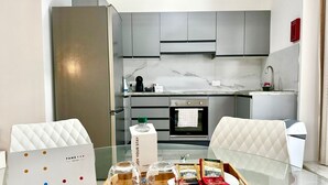 Une cuisine moderne avec des meubles gris, un réfrigérateur en acier inoxydable et une table à manger en verre, sur laquelle se trouvent un plateau avec des sachets de thé et des verres.
