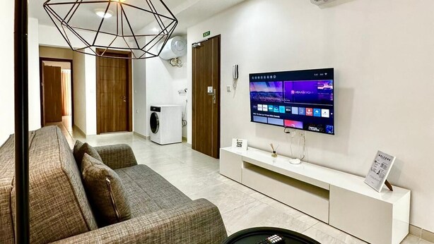 Un salon moderne avec un canapé, une table basse noire, un téléviseur fixé au mur et un luminaire suspendu au design géométrique original.
