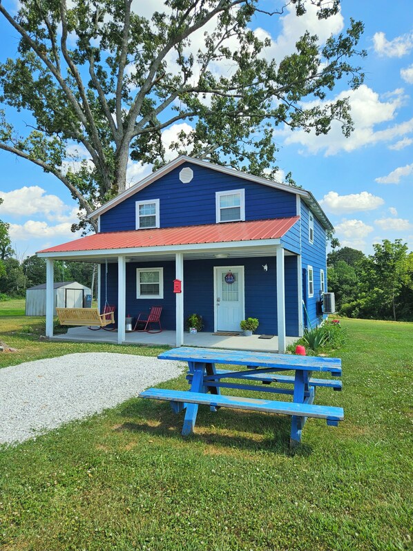 Une maison bleue avec un porche, une balançoire et une table de pique-nique.