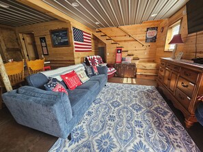 L’intérieur d’une cabane en rondins, avec un canapé bleu, un tapis à motifs, une commode en bois et des décorations à l’effigie du drapeau américain.