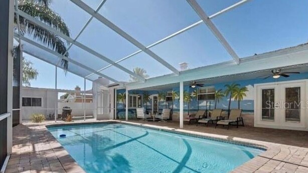 A swimming pool with a glass enclosure, lounge chairs, and a mural of palm trees. - Tropical Oasis with Private Pool & Modern Comforts – Minutes to Beach! (Largo)