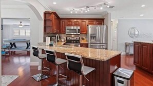 A modern kitchen with dark wooden cabinets, stainless steel appliances, and a central island with bar stools. - Tropical Oasis with Private Pool & Modern Comforts – Minutes to Beach! (Largo)
