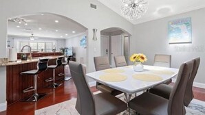 A modern kitchen with a bar area, a dining table with chairs, and a chandelier. - Tropical Oasis with Private Pool & Modern Comforts – Minutes to Beach! (Largo)