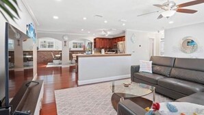 A spacious living room with a dark leather sofa, a glass coffee table, and a ceiling fan. - Tropical Oasis with Private Pool & Modern Comforts – Minutes to Beach! (Largo)