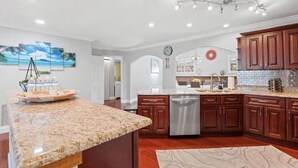 A kitchen with granite countertops, wooden cabinets, a dishwasher, and a decorative island. - Tropical Oasis with Private Pool & Modern Comforts – Minutes to Beach! (Largo)