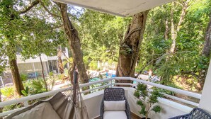 A balcony with a hammock, two wicker chairs, and a potted plant.