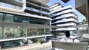 A modern building with multiple floors, glass storefronts, and a balcony with a chair.