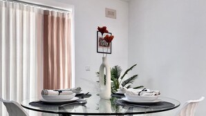 A modern dining area with a glass table, white chairs, and a vase with red flowers.