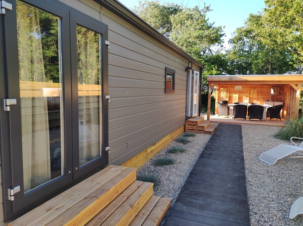 A modern cabin with large sliding glass doors, a wooden deck, and a cozy outdoor seating area with a grill.