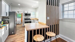 A modern kitchen with a wooden island, stainless steel appliances, and a view of the outdoors. - University Heights Renovated Home -King bed ,4-bedroom with WIFI, fitness room (University Heights)