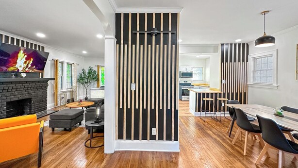 A modern living room with a fireplace, a dining area with a wooden table and chairs, and a kitchen in the background. - University Heights Renovated Home -King bed ,4-bedroom with WIFI, fitness room (University Heights)