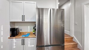 A compact kitchen with white cabinets, a stainless steel refrigerator, a coffee maker, and a cutting board on the countertop. - University Heights Renovated Home -King bed ,4-bedroom with WIFI, fitness room (University Heights)