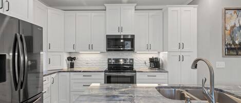 A modern kitchen with white cabinets, stainless steel appliances, a marble countertop, and a pendant light.