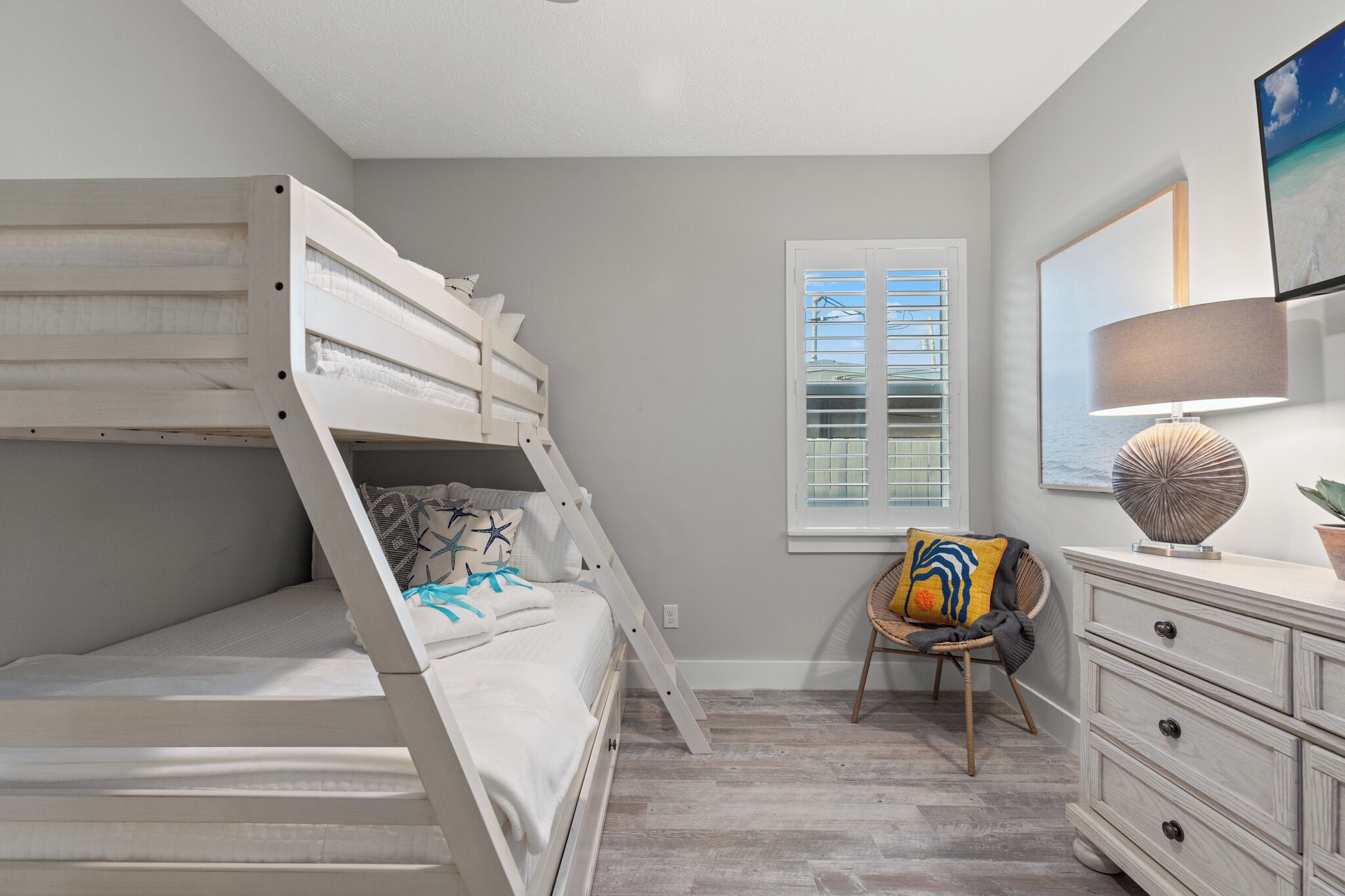 Une chambre avec un lit superposé, une fenêtre avec des stores, une chaise, une commode et une lampe.