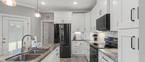 A modern kitchen with white cabinets, stainless steel appliances, a double sink, and pendant lighting.