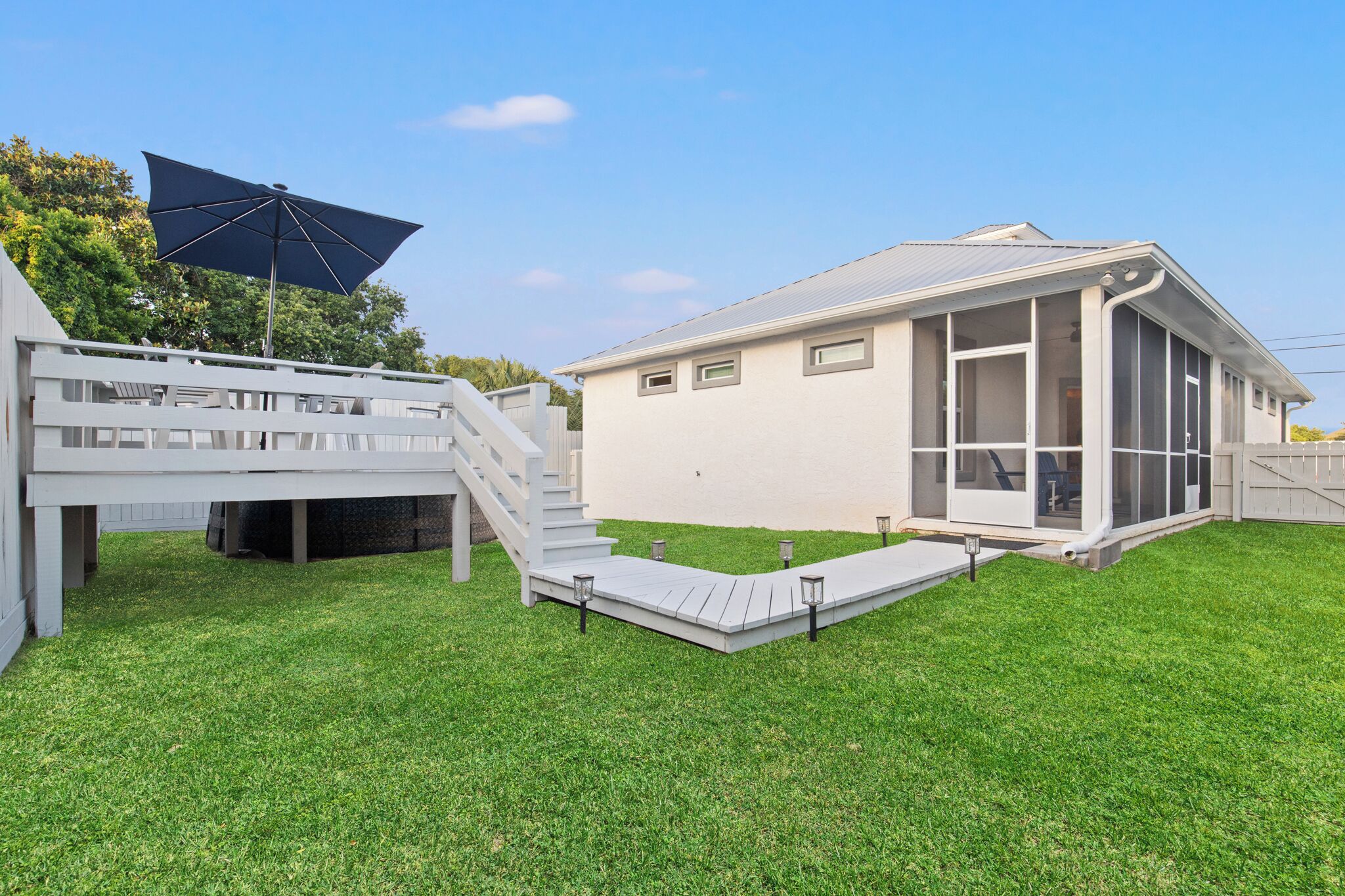 A modern house with a covered patio, a staircase, and a well-maintained lawn.