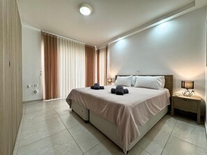 A modern hotel room with a large bed, a bedside table with a lamp, and a window with curtains.