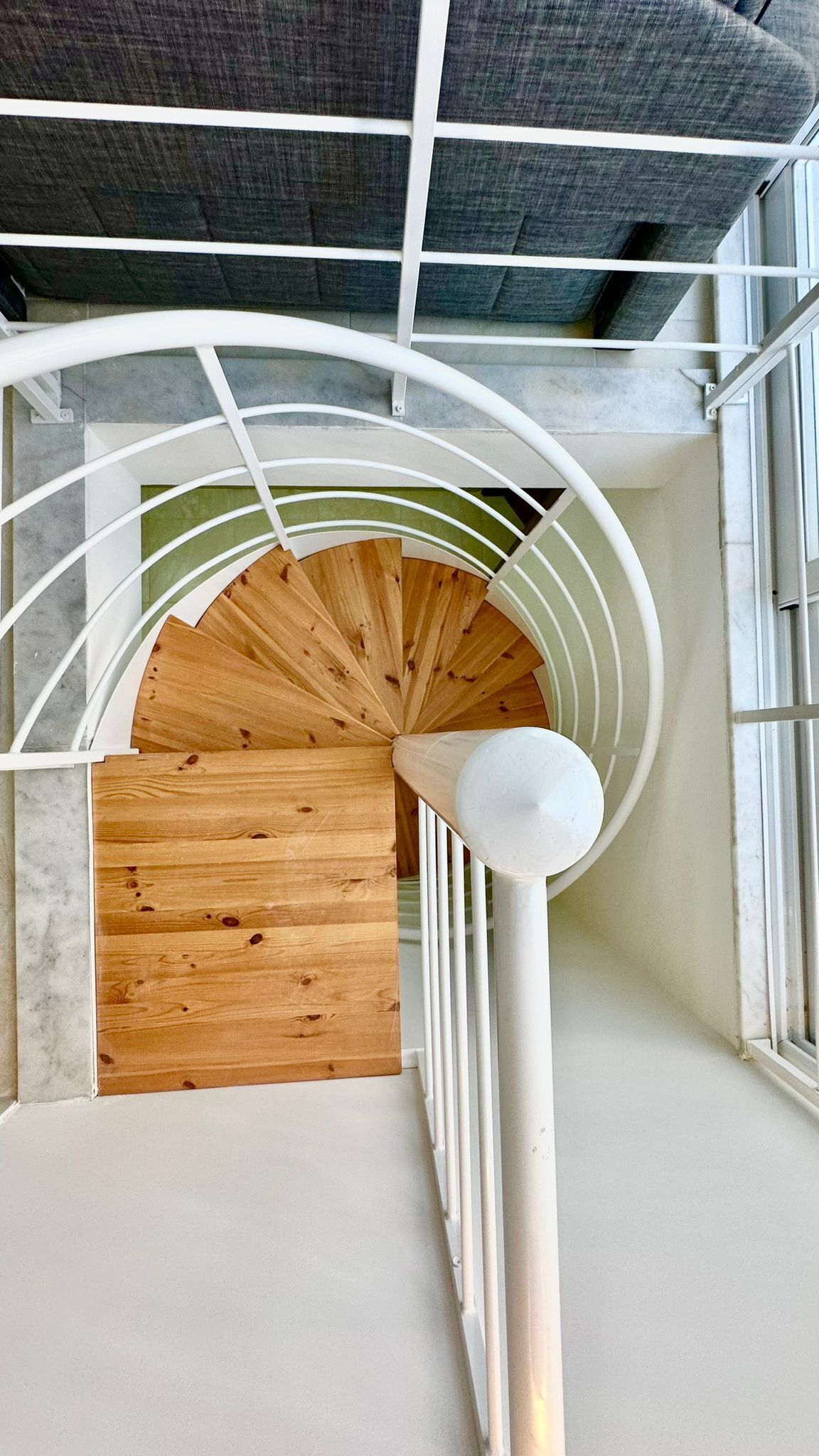 Una escalera de caracol con detalles de madera y barandillas blancas, que conduce a un techo con diseño de cuadrícula.