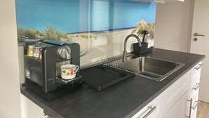 A compact kitchenette with a coffee maker, a sink, and a window with a beach view.