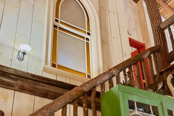 Un escalier en bois avec une rampe, une fenêtre à cadre blanc et un meuble vert.