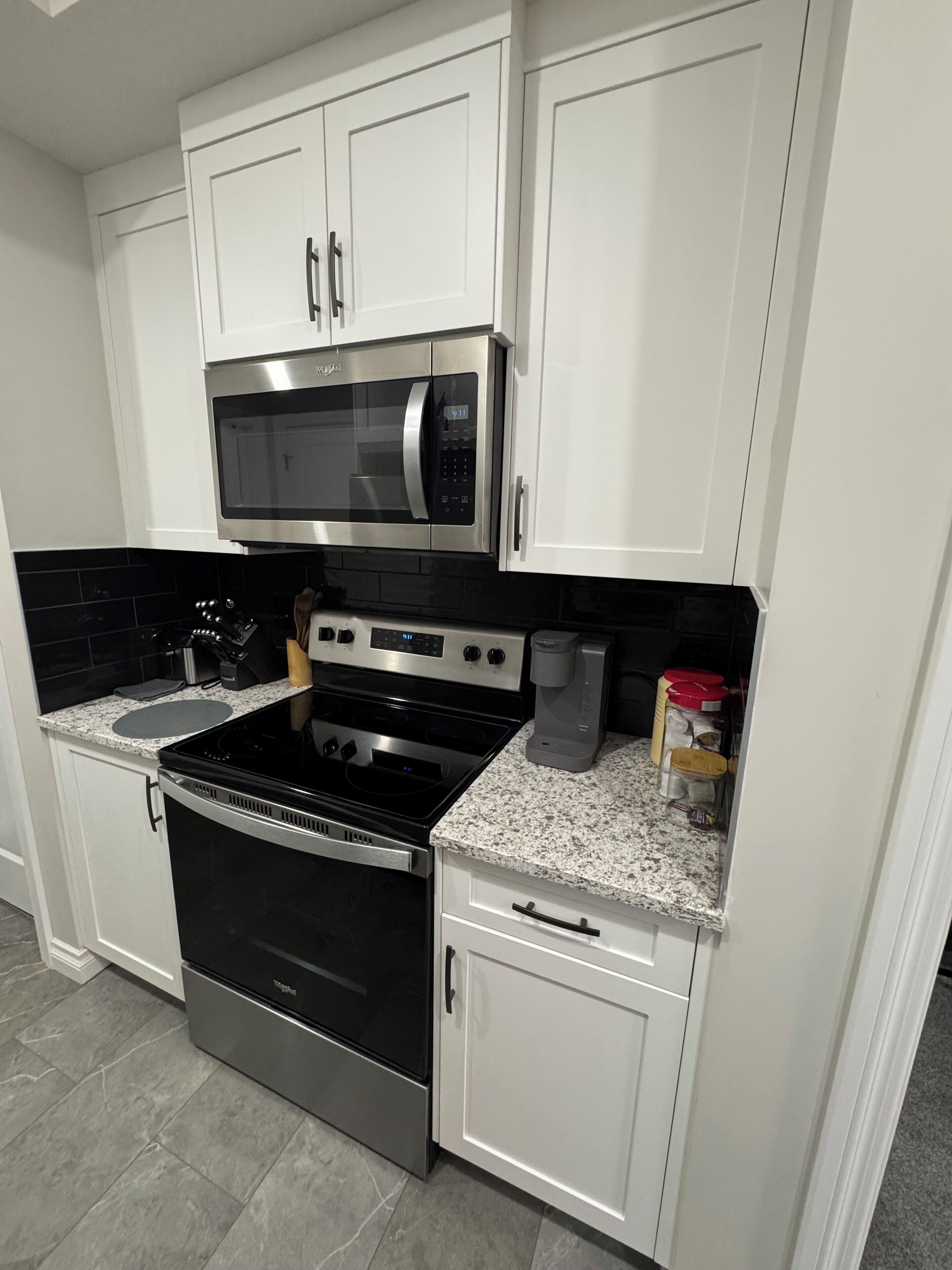 A kitchen with white cabinets, a stainless steel microwave, a stove, and a coffee maker.