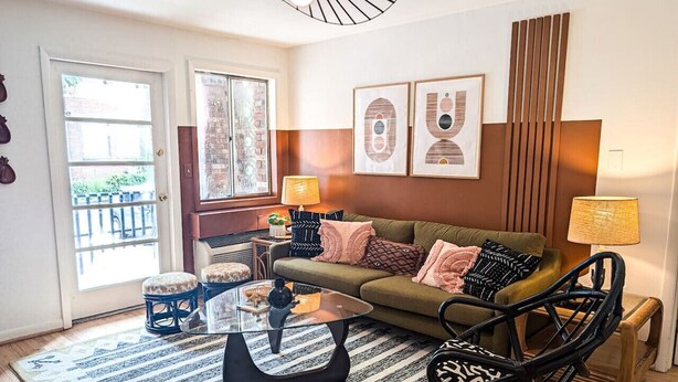 Een woonkamer met een bank, salontafel en een rotan stoel. Er is een deur met ruitpanelen en uitzicht op het exterieur.