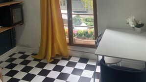 A room with a checkered floor, a window with a yellow curtain, a white table, and a chair. - Room in Montmartre with privat bathroom (Paris)