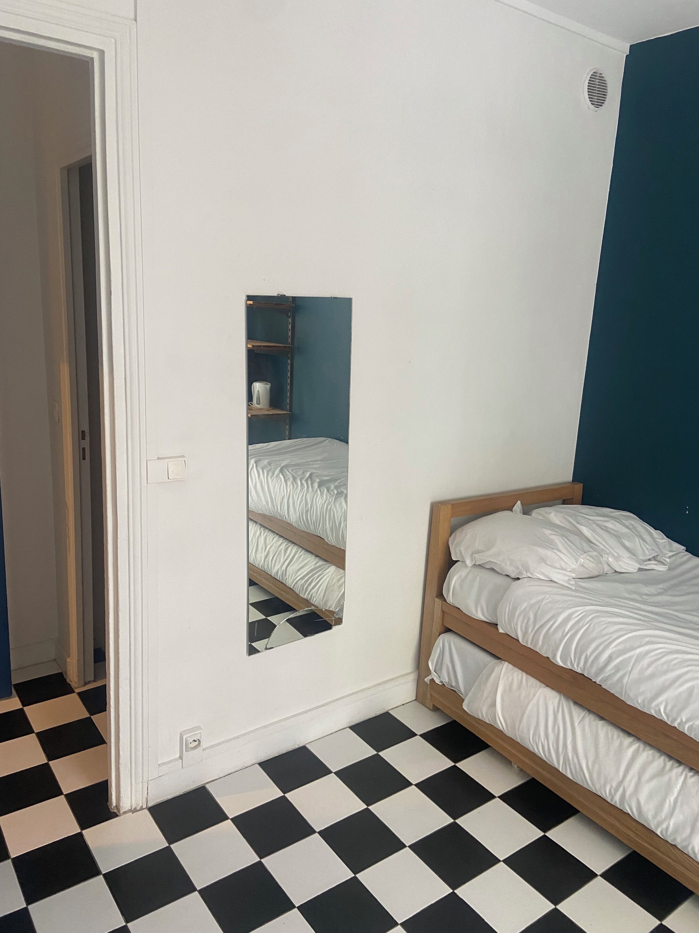 A room with a checkered floor, a wooden bed, a mirror, and a blue wall.