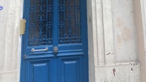 A blue door with a glass upper section and decorative metalwork, set in a building with a white facade and a number '24' sign. - Room in Montmartre with privat bathroom (Paris)