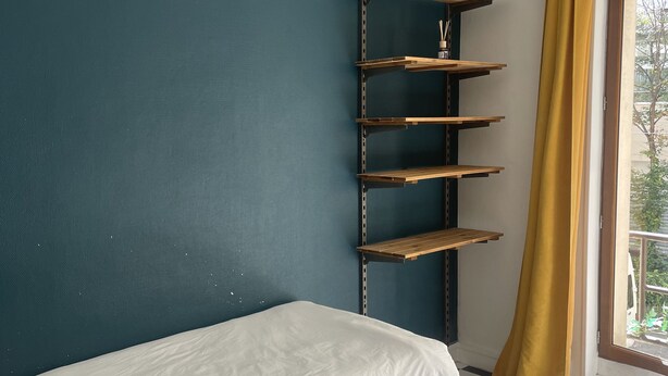 A room with a single bed, a metal shelf unit, a checkered floor, and a window with a yellow curtain. - Room in Montmartre with privat bathroom (Paris)