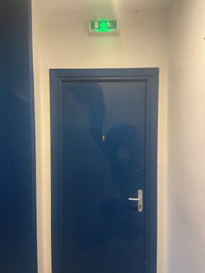 A closed door with a visible handle and a green emergency exit sign above it.