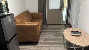 A compact living space with a kitchenette, a brown sofa, a dining table with a bowl, and a sliding glass door leading outside.