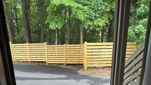 A door with a doormat that reads "welcome goodbye" and a view of a parking lot with a wooden fence and trees in the background.