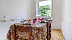 A dining area with a table set for four, a window with a view of greenery, and a patterned tablecloth.