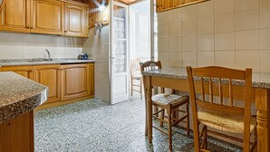A kitchen with wooden cabinets, a granite countertop, a dining table with chairs, and a tiled floor.