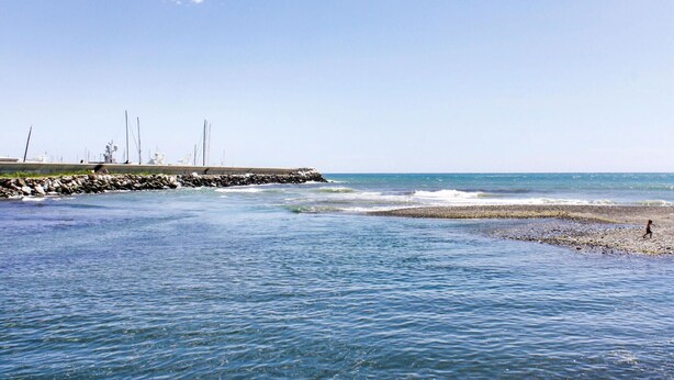 A coastal scene with a rocky shoreline, calm sea, and a person walking on the beach.