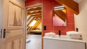 A bedroom with a sloped ceiling, a bed, and a bathroom with a sink and towels.
