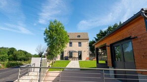 A two-story house with a stone facade, a wooden extension, and a paved driveway leading to a gated entrance.