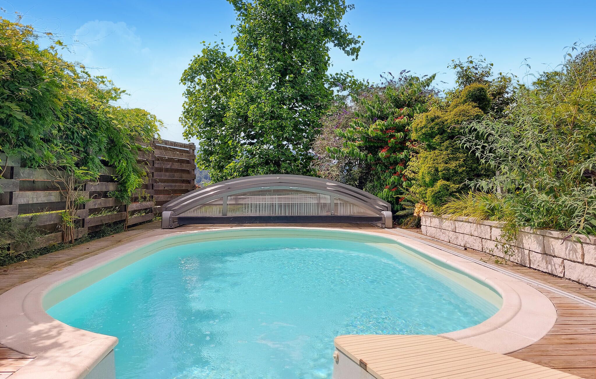Una piscina con plataforma de madera y zona cubierta.