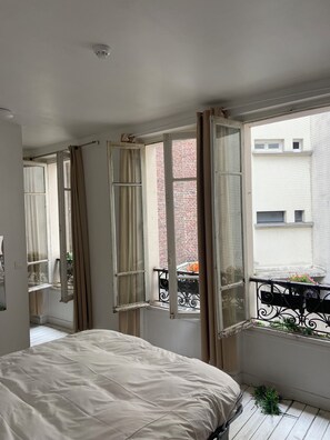 A bedroom with a large bed, an open window, and a view of a brick building outside.